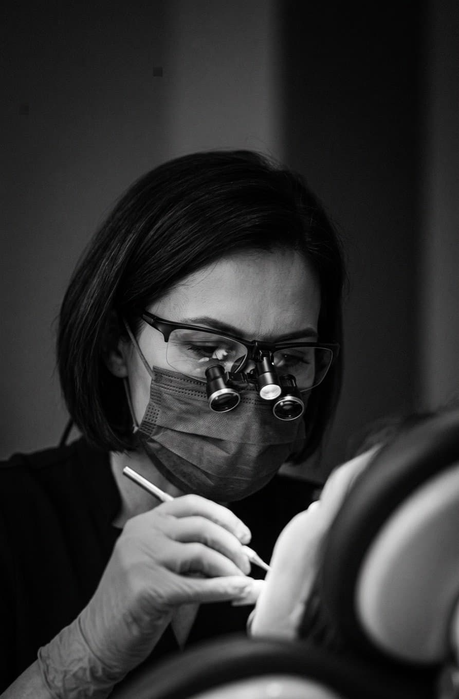 Dentista com lupas cirúrgicas e máscara em atendimento, foto em preto e branco